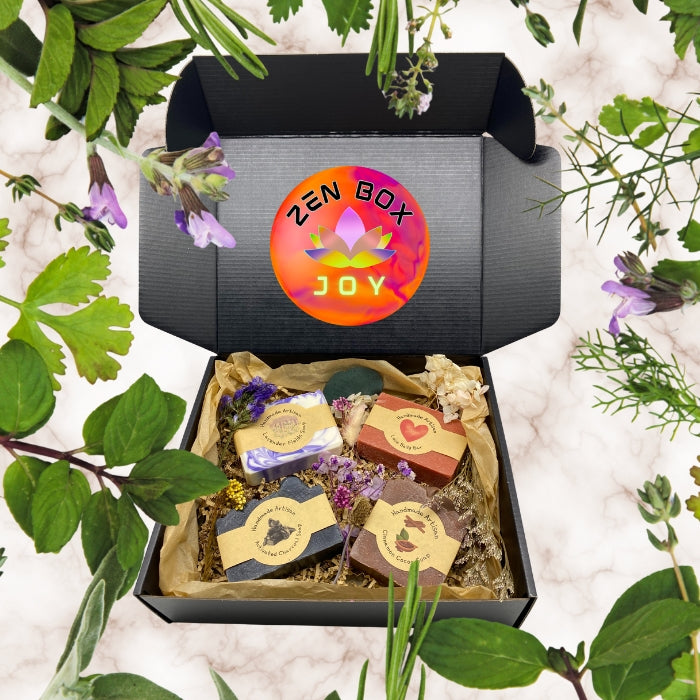 Open subscription box labeled 'ZEN BOX JOY' with handmade soap bars and herbs on a white background with greenery.